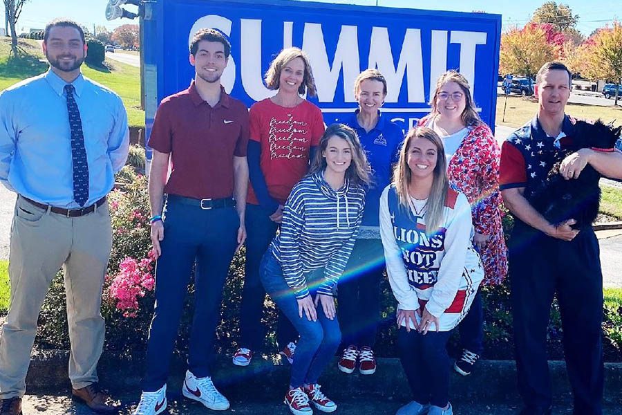 Community Involvement - Summit Insurance Group Inc Team Standing Together in Front of Their Company Signage on a Sunny Day