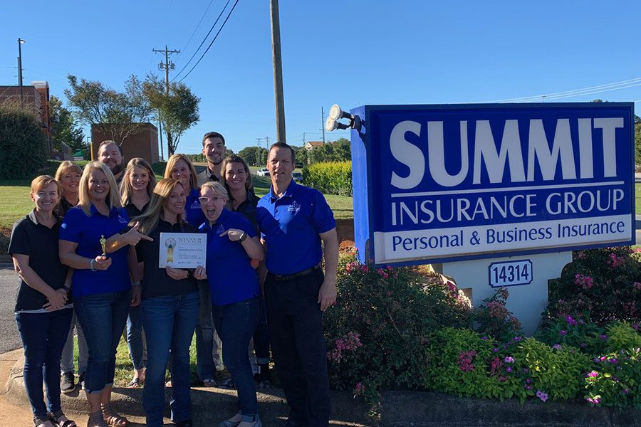 Community Involvement - Summit Insurance Group Inc Team Standing Together in Next to Their Company Signage Holding an Award on a Sunny Day